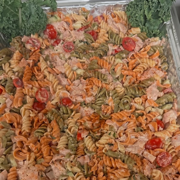 Colorful pasta salad with cherry tomatoes, chicken, and kale in a catering tray.