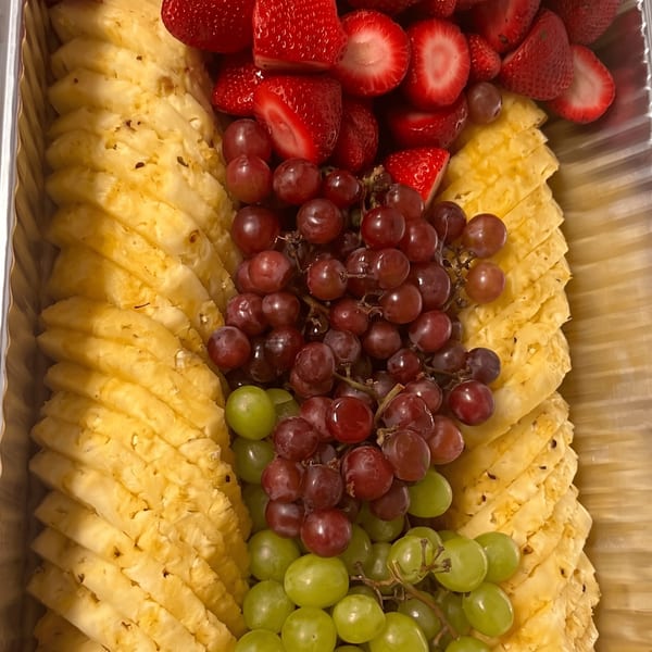A vibrant fruit platter with sliced pineapple, red strawberries, and red and green grapes.
