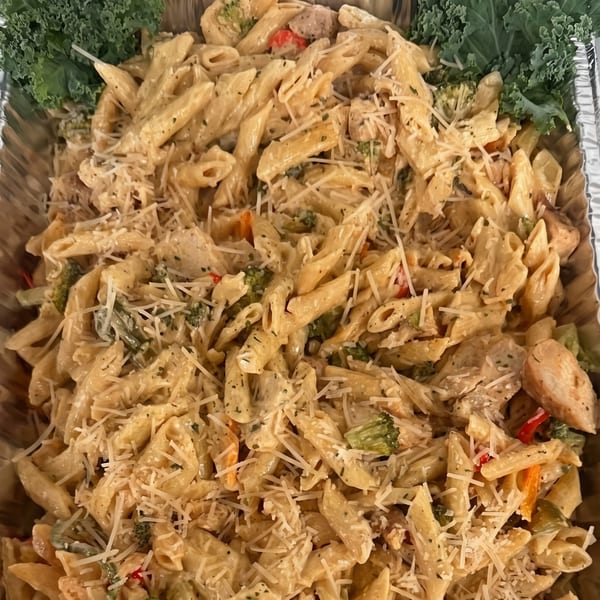Creamy penne pasta with chicken, broccoli, red peppers, and shredded Parmesan cheese in a foil tray.