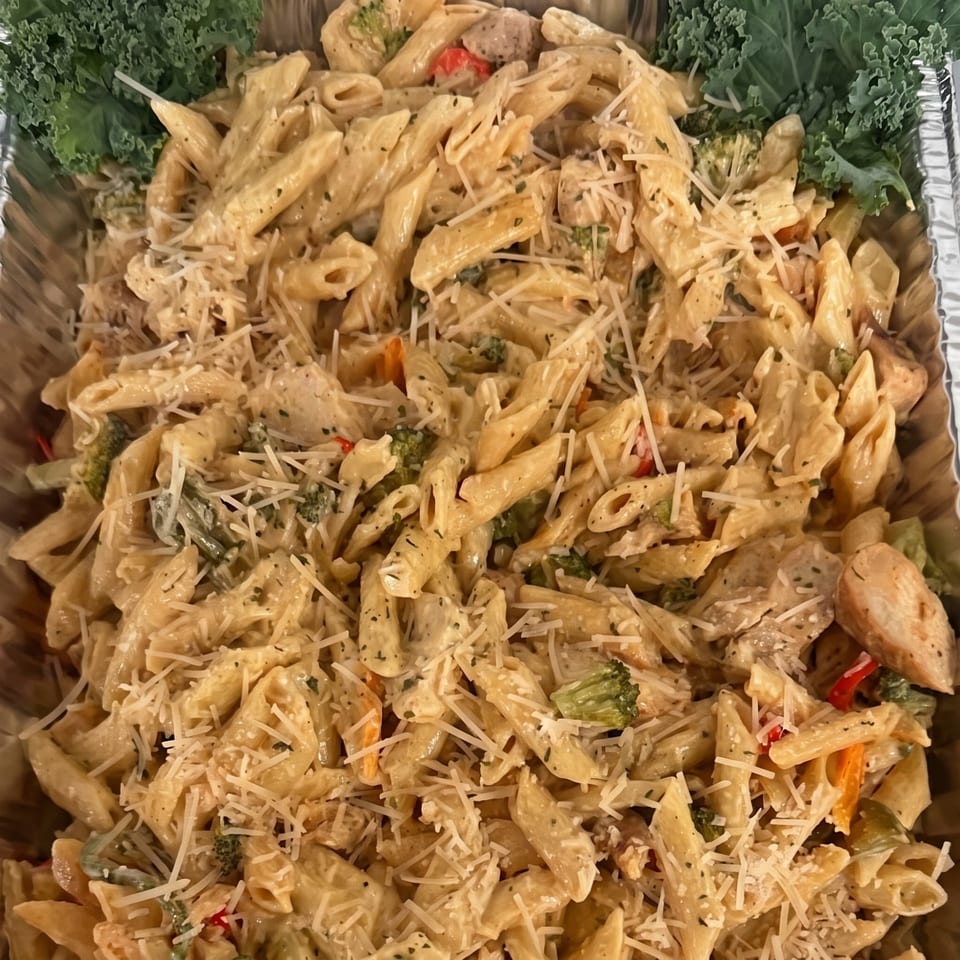 Creamy penne pasta with chicken, broccoli, red peppers, and shredded Parmesan cheese in a foil tray.