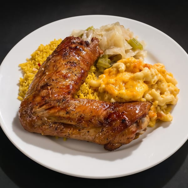 Glazed turkey wing with yellow rice, macaroni and cheese, and stewed cabbage on a white plate.